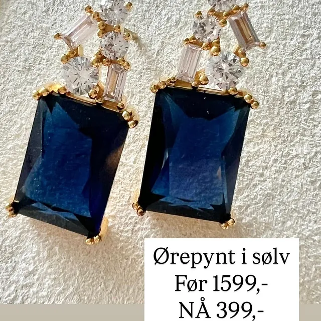 Et par hengende øredobber med store, rektangulære mørkeblå edelstener nederst, og klynger av små blanke stener øverst.